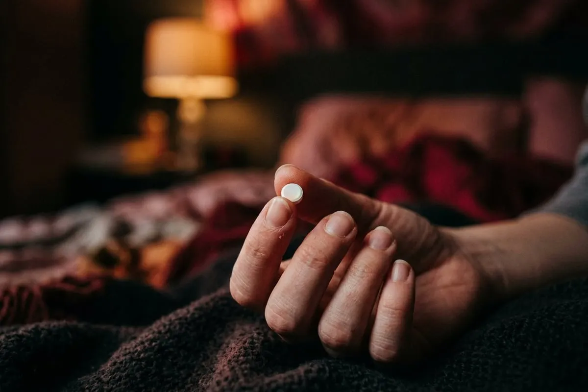 女性手指輕捏一顆避孕藥，柔和琥珀色光從後方打亮，氛圍沉靜