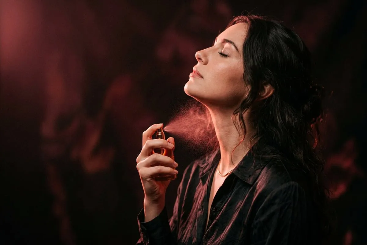 女人側臉仰頭輕噴香水，細緻噴霧在暗玫瑰光中浮現，側面構圖